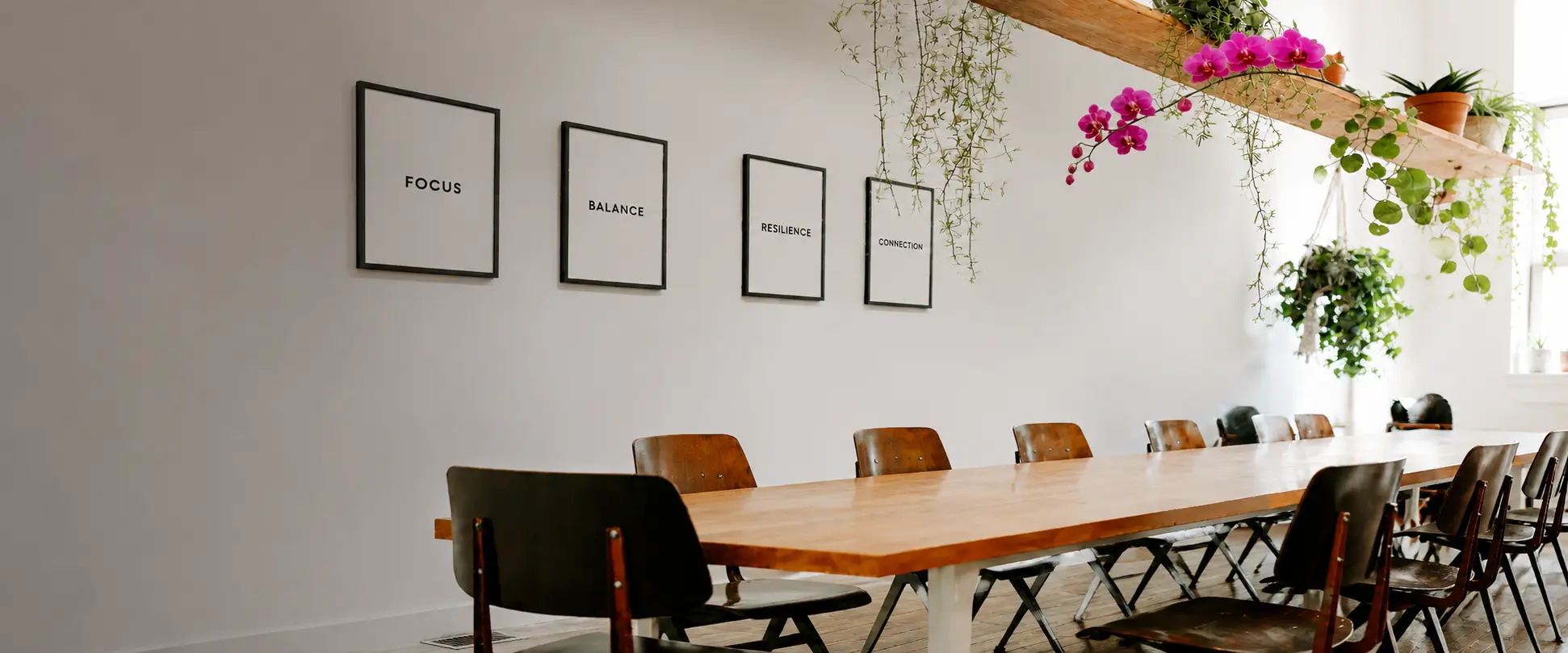 Bright corporate wellness meeting room with a clean conference table, Focus, Balance, Resilience, and Connection in black frames, and a visible fuchsia orchid